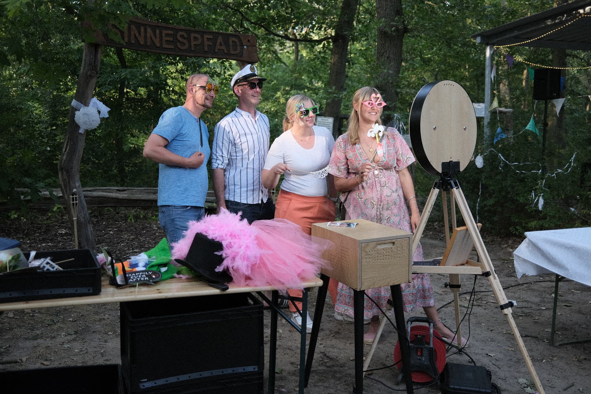 Vier Gäste mit Requisiten posieren vor der Fotobox im Wald